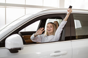 Auto business, car sale, consumerism and people concept. Happy Caucasian woman taking car key from dealer in bright showroom or salon and showing them to camera.