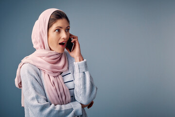 Surprised, phone call and muslim woman with smartphone in studio for shock, wow or omg reaction on blue background. Hijab, amazed and Arab person with wtf expression for gossip, fake news or secret - obrazy, fototapety, plakaty