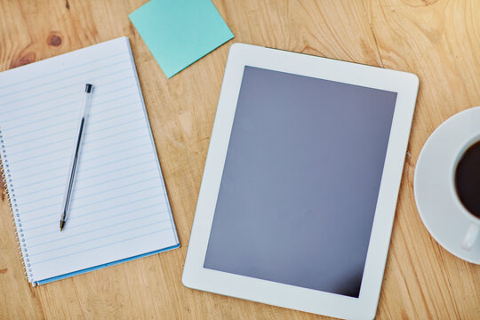 High angle, desk and tablet or paper in closeup with coffee, workspace with technology for background. Notebook, epad and above on table with drink in zoom, internet or app for marketing business