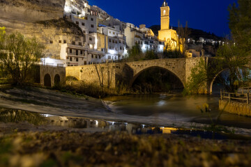 Alcalá del Júcar at night, located on a rock formed by the gorge of the Júcar River, cave houses roman bridge, castle, Church of San Andrés Apóstol (Albacete, Spain).