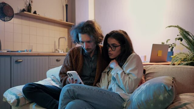 Couple engrossed in smartphone in cozy home interior.