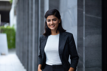 Indian Asian business woman - Portrait Smiling Young Businesswoman in black suit at outside modern office building. Positive human emotions