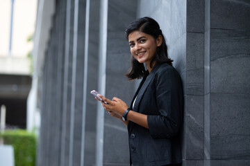 Mobile phone technology lifestyle - Portrait Smiling Young Businesswoman in black suit using smartphone at outside modern office building
