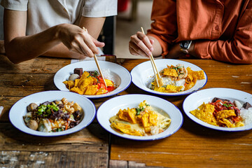 Young Asian couple traveler tourists eating Thai street food together in Laplae District market in Uttaradit Province, Thailand - people traveling enjoying food culture concept.
