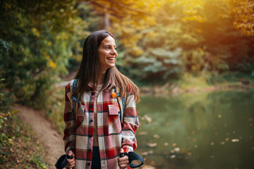 Naklejka na ściany i meble Happy woman with a backpack spending a day in nature, a portrait. Young woman hiking and going camping in nature. Person with backpack walking in the forest