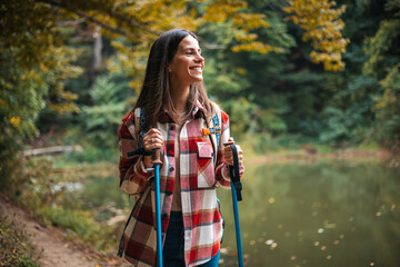 Beautiful woman traveler climbs uphill with a dog on a background of mountain views. She is with a backpack and in red clothes. Woman in the forest hiking with hiking poles - 786263331