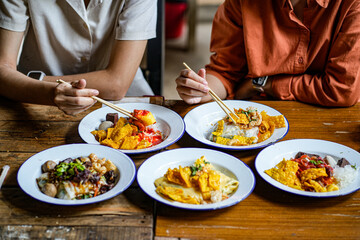 Young Asian couple traveler tourists eating Thai street food together in Laplae District market in Uttaradit Province, Thailand - people traveling enjoying food culture concept.
