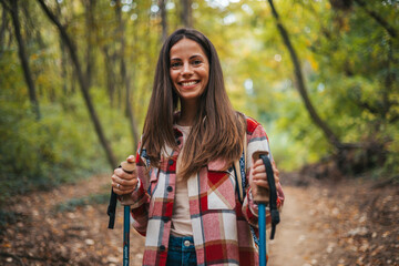 Beautiful woman traveler climbs uphill with a dog on a background of mountain views. She is with a backpack and in red clothes. Woman in the forest hiking with hiking poles - 786263902