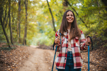 Beautiful woman traveler climbs uphill with a dog on a background of mountain views. She is with a backpack and in red clothes. Woman in the forest hiking with hiking poles - 786263980