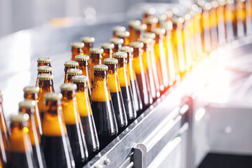 Brown glass beer bottles on conveyor belt Automated brewery industry manufacturing with sunlight
