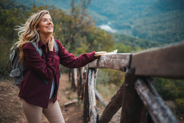 Photo of a young smiling woman carrying a backpack and hiking in the nature. Young woman breathing pure air in a forest. Happy hiker caucasian woman smile and enjoy the nature walking - 786265142