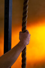 close-up in sports club of a hand holding ropes for exercise on a bright orange background