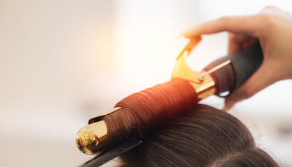 Woman hairdresser stylist skillfully curling hair with golden iron in salon