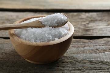 Organic salt in bowl and spoon on wooden table, closeup. Space for text