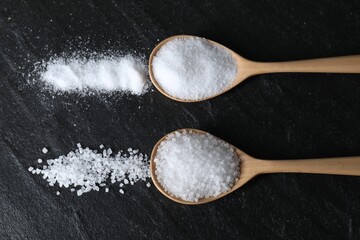 Organic salt in spoons on black table, flat lay