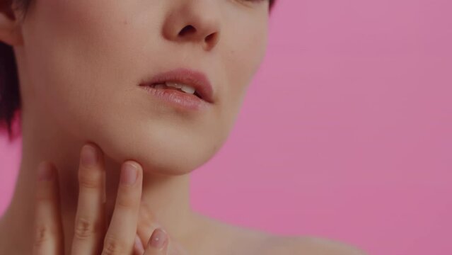 Young beautiful woman with clean skin touching her cheeks with both hands on a pink background close up. Concept of skin care for health and beauty