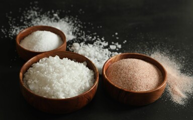 Different types of organic salt in bowls on black table, closeup