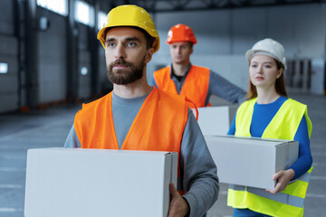 Group of workers, loaders, wearing hard hats and work uniforms, hold boxes, mockup looking away