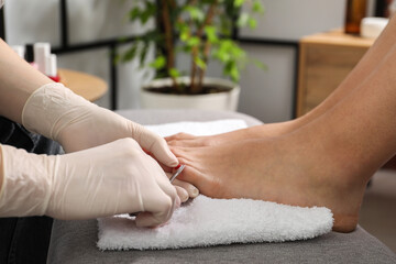 Pedicurist cutting client`s toenails with scissors in beauty salon, closeup