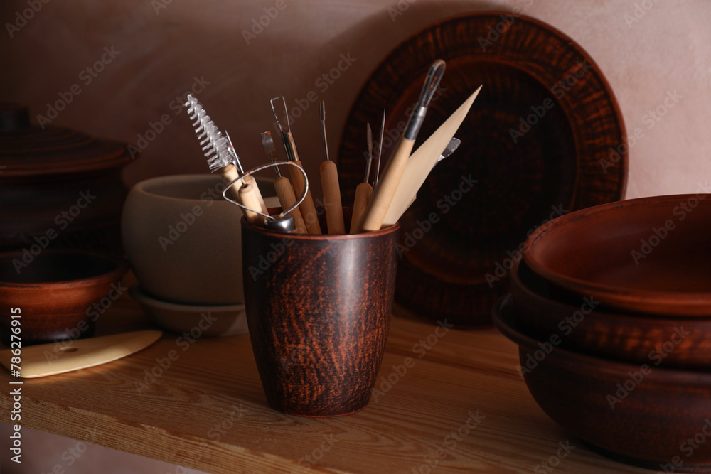 Wall mural Set of different crafting tools and clay dishes on wooden table in workshop