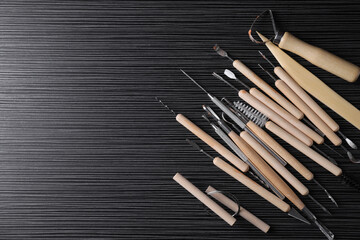 Clay and set of modeling tools on dark gray wooden table, flat lay. Space for text