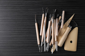 Clay and set of modeling tools on dark gray wooden table, flat lay. Space for text