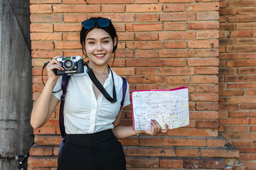 Portrait happy young Female tourist holding city map and camera exploring Tha pae Gate during...