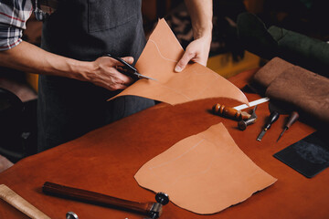 Leather artisan using scissors tool on workbench for product in workshop
