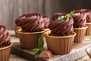Delicious cupcakes with chocolate pieces and mint on wooden table, closeup