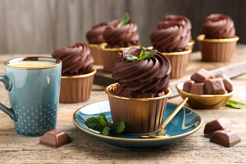 Delicious cupcakes with chocolate pieces and mint on wooden table