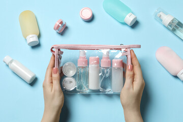 Cosmetic travel kit. Woman with plastic bag and small containers of personal care products on light...