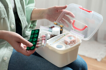 Woman putting pills into first aid kit indoors, closeup