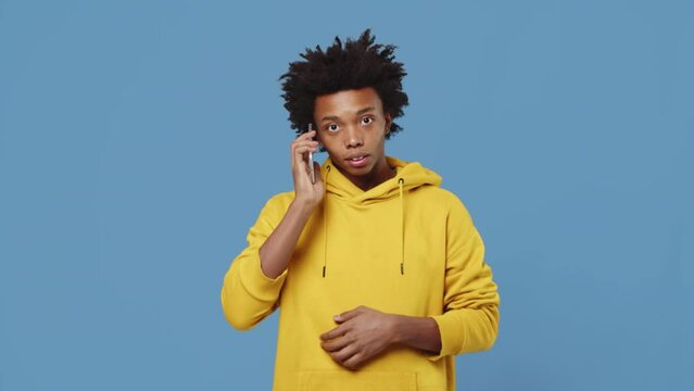 Young black guy standing and typing a phone number on a smartphone and starts to talk with a friend with a smiling face on a blue background in the studio