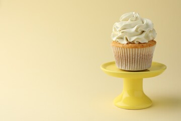 Tasty vanilla cupcake with cream on pale yellow background, space for text