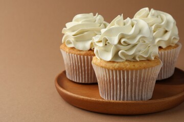 Tasty vanilla cupcakes with cream on dark beige background, closeup. Space for text