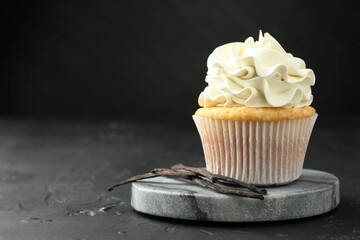 Tasty cupcake with cream and vanilla pods on black table, closeup. Space for text