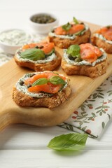 Tasty canapes with salmon, capers and sauce on white wooden table