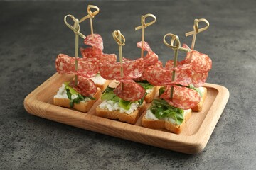 Tasty canapes with salami, greens and cream cheese on grey table