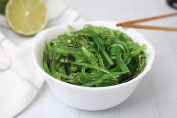Tasty seaweed salad in bowl served on white tiled table, closeup