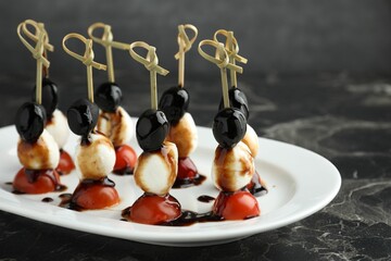 Tasty canapes with black olives, mozzarella and cherry tomatoes on dark textured table, closeup