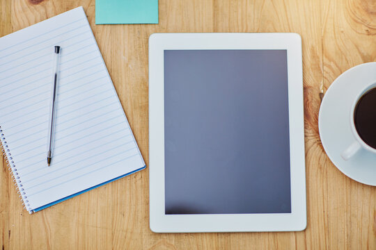 High angle, desk and tablet or paper in zoom with coffee, workspace with technology for background. Notebook, epad and above on table with drink in closeup, internet or app for marketing business