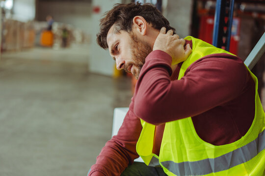 Tired upset, sick bearded man, worker having neck and back pain, after work in warehouse, copy space