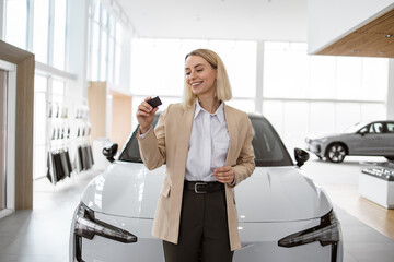 Happy smiling business lady standing near new bought car and hugging keys in car dealership....