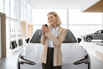 Happy smiling business lady standing near new bought car and hugging keys in car dealership....