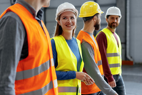 Confident woman wearing hard hat and vest talking to her colleagues while walking around warehouse - Powered by Adobe
