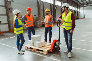 Group of successful managers, workers wearing safety helmet and vest loading boxes on pallet truck
