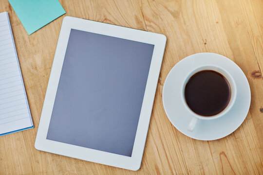 High angle, table and tablet or coffee in closeup with paper, workspace with technology for background. Notebook, epad and above on desk with drink in zoom, internet or app for marketing business