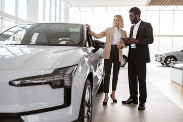 Successful businesswoman in car showroom sale of vehicles to customers. African male consultant...