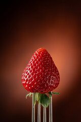 fork holds a single strawberry in the foreground on a black background with red glow - 786293732