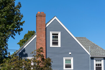 Home facade with gable roof, blue siding and brick chimney in Brighton, Massachusetts, USA